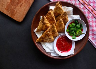 Samosa, samsa veya somsa, siyah arka planda domates sosu ve pırasa dilimi ile servis edilen üç köşeli kızarmış hamur işidir.