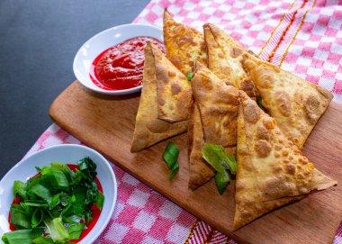 Samosa, samsa veya somsa, siyah arka planda domates sosu ve pırasa dilimi ile servis edilen üç köşeli kızarmış hamur işidir.