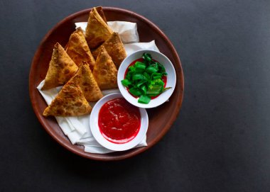 Samosa, samsa veya somsa, siyah arka planda domates sosu ve pırasa dilimi ile servis edilen üç köşeli kızarmış hamur işidir.