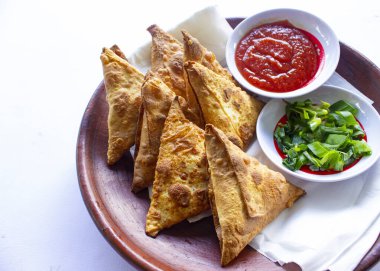 Samosa, samsa veya somsa, siyah arka planda domates sosu ve pırasa dilimi ile servis edilen üç köşeli kızarmış hamur işidir.