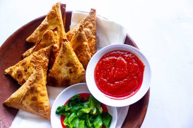 Samosa, samsa veya somsa, siyah arka planda domates sosu ve pırasa dilimi ile servis edilen üç köşeli kızarmış hamur işidir.