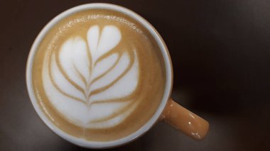 Kahverengi arka planda seçici odaklı bir kadın eli olan sıcak kahve kapuçino bardağı.