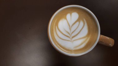 Kahverengi arka planda seçici odaklı bir kadın eli olan sıcak kahve kapuçino bardağı.