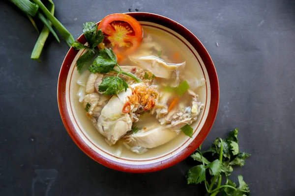 Chicken soup served with vegetables, tomatoes, celery in a bowl, spoon and fork. with black background