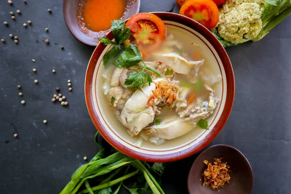 Chicken soup served with vegetables, tomatoes, celery in a bowl, spoon and fork. with black background