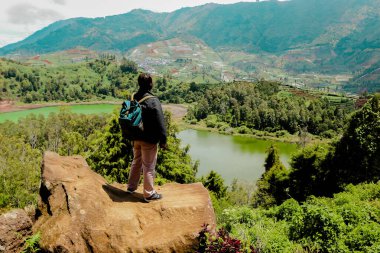 Genç adam uçurumun kenarında duruyor ve gölün ve dağın manzarasının tadını çıkarıyor. Özgürlüğün sembolü.