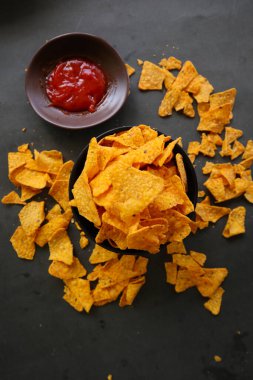 Tortilla cipsi, mısır cipsidir veya mısır cipsi olarak adlandırılır, kasede servis edilir, mısırdan yapılan siyah arka planda.