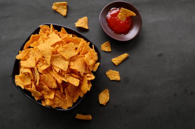 Tortilla cipsi, mısır cipsidir veya mısır cipsi olarak adlandırılır, kasede servis edilir, mısırdan yapılan siyah arka planda.