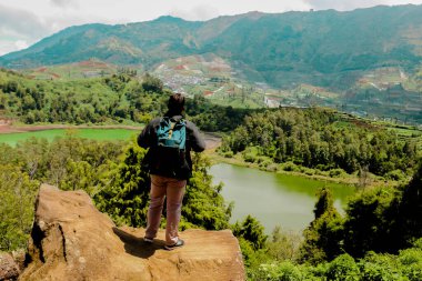 Genç adam bir kayanın üzerinde duruyor ve göl ve dağ manzarasının tadını çıkarıyor. Özgürlüğün sembolü