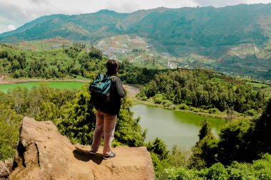 Genç adam uçurumun kenarında duruyor ve gölün ve dağın manzarasının tadını çıkarıyor. Özgürlüğün sembolü.