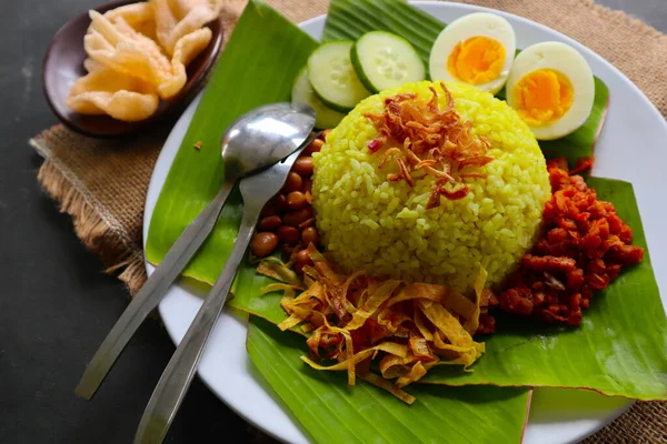 nasi kuning or yellow rice or tumeric rice is traditional food from asia, made rice cooked with turmeric, coconut milk and spices served with egg, chicken, peanuts, chili sauce, sliced cucumber