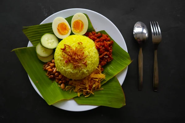 nasi kuning or yellow rice or tumeric rice is traditional food from asia, made rice cooked with turmeric, coconut milk and spices served with egg, chicken, peanuts, chili sauce, sliced cucumber