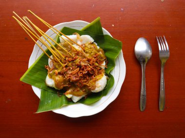 Sate Padang or satay padang is Spicy beef satay from Padang, West Sumatra. Served with spicy curry sauce and rice cake, lontong on banana leaf. isolated on white background