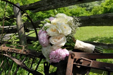 Close up of White Rose and Pink Peonies Wedding Bouquet on Rusty Farm Equipment clipart