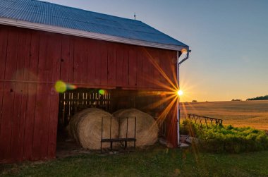 Sunset 'te Red Barn Depolanmış Yuvarlak Hay Bails İçerde ve Arkaplanda Buğday Tarlası