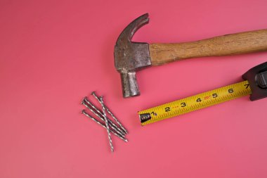 Çekiç, çivi ve mezuranın düzleşmesi Pembe bir arkaplanda izole edildi