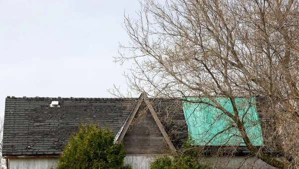 Residential Roof in Desperate Need of Repair or Replacement with peeling shingles and Tarp