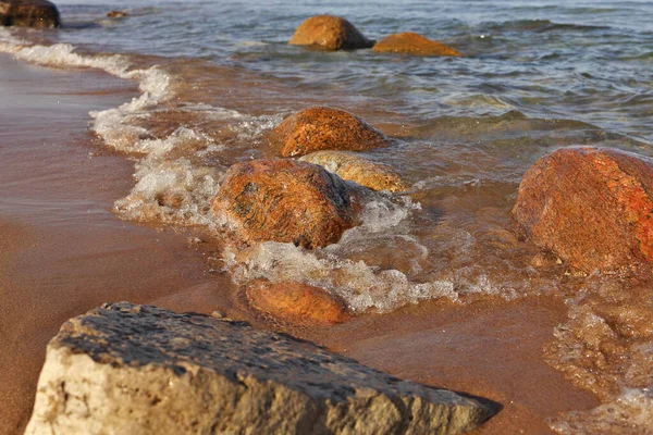Disparo de ángulo bajo de pequeñas olas rodando en la playa salpicada de rocas coloridas y rocas — Foto de Stock