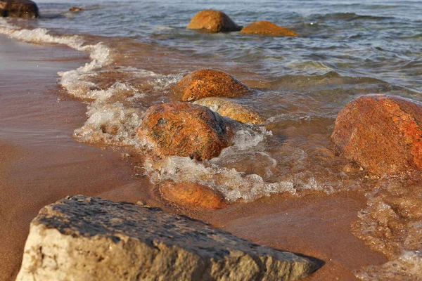 Low Angle Shot of Small Waves Rolling into Beach Dotted with Colorful Rocks and Boulders — стоковое фото