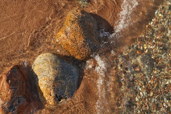 Direkt ovanför skott av små vågor rullar in i stranden prickad med färgglada stenar och block — Stockfoto