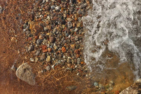 Small Waves Rolling into Sandy Beach Dotted with Colorful Pebbles, Rocks, and Stones — стоковое фото