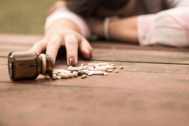 Kadın aşırı dozda ilaç alıyor ve açık ilaç şişesiyle ahşap masada yatıyor.