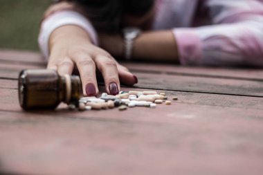 Kadın aşırı dozda ilaç alıyor ve açık ilaç şişesiyle ahşap masada yatıyor.