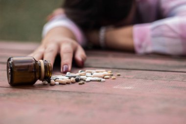 Kadın aşırı dozda ilaç alıyor ve açık ilaç şişesiyle ahşap masada yatıyor.