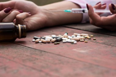 Kadın aşırı dozda ilaç alıyor ve açık ilaç şişesiyle ahşap masada yatıyor.