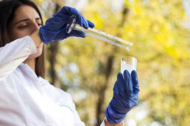 Test tüplü, açık havada, arka planda kadın kimyager.