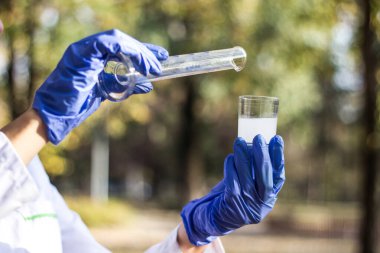 Test tüplü, açık havada, arka planda kadın kimyager.