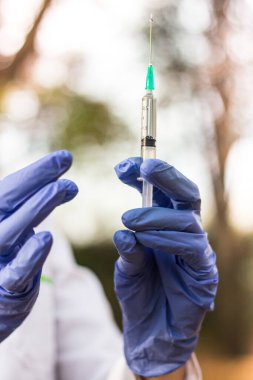 Kadın doktor elinde şırınga tutuyor. Şırıngayla çekilen bir şişedeki aşı.