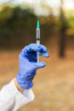 Kadın doktor elinde şırınga tutuyor. Şırıngayla çekilen bir şişedeki aşı.