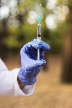 Kadın doktor elinde şırınga tutuyor. Şırıngayla çekilen bir şişedeki aşı.