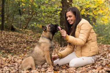 Mutlu, gülümseyen bir kadın. Köpeğini kucaklıyor, parkta uzanıyor.