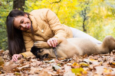 Mutlu, gülümseyen bir kadın. Köpeğini kucaklıyor, parkta uzanıyor.