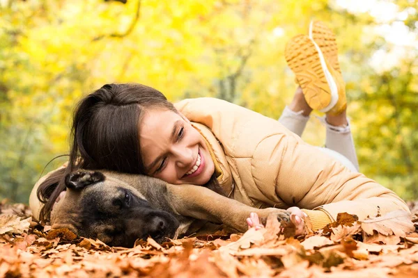 Mutlu, gülümseyen bir kadın. Köpeğini kucaklıyor, parkta uzanıyor.