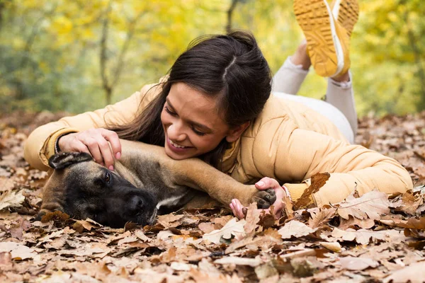 Mutlu, gülümseyen bir kadın. Köpeğini kucaklıyor, parkta uzanıyor.