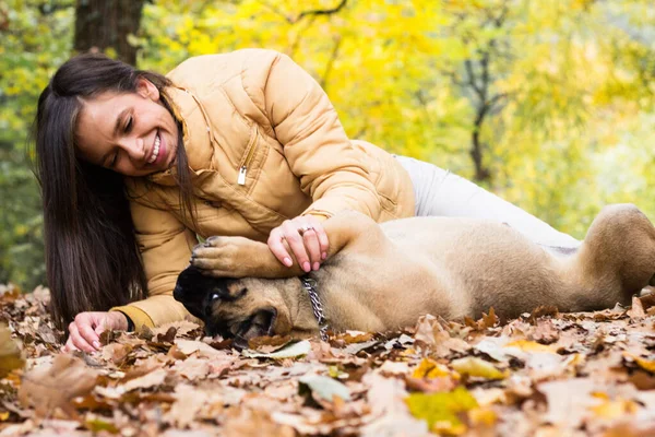 Mutlu, gülümseyen bir kadın. Köpeğini kucaklıyor, parkta uzanıyor.