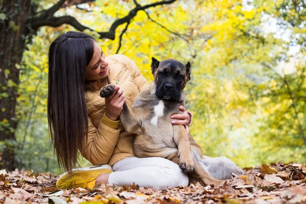 Mutlu, gülümseyen bir kadın. Köpeğini kucaklıyor, parkta uzanıyor.