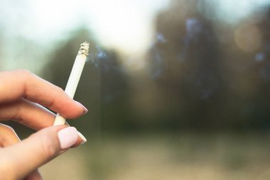 Sigara içen genç bir kadın. Sigara tutarken, arka planda...