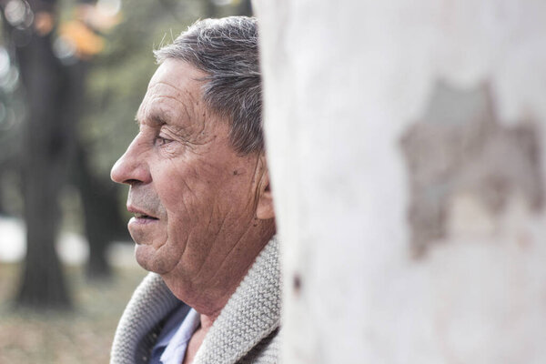 Old man relaxing outdoors and looking down. Portrait of senior man looking thoughtful