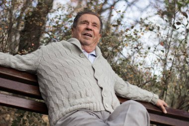 Açık hava parkında bankta oturan gülümseyen son sınıf öğrencisinin portresi. Yaşlı adam dışarıda dinleniyor ve kameraya bakıyor. Emekliliğin tadını çıkaran yaşlı bir adamın portresi