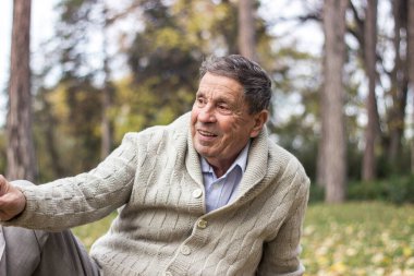 Portrait of happy senior man smiling, in the public park, outdoors.. Old man relaxing outdoors and looking away and sitting down. Portrait of elderly man enjoying retirement clipart