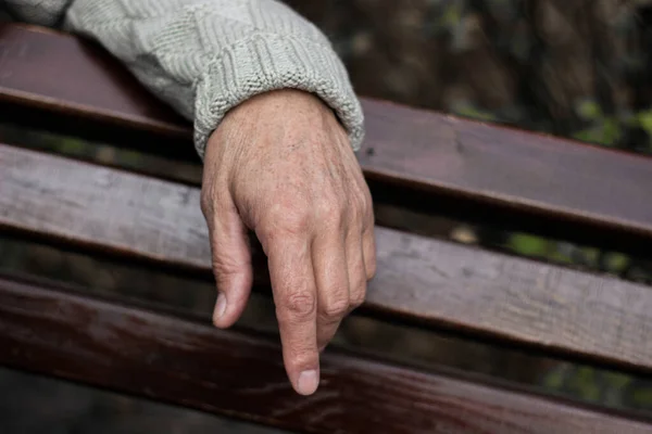 The lonely older hand of a man. An older man sitting on a bench, bokeh background, outdoors