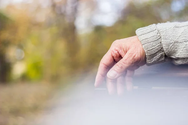 The lonely older hand of a man. An older man sitting on a bench, bokeh background, outdoors