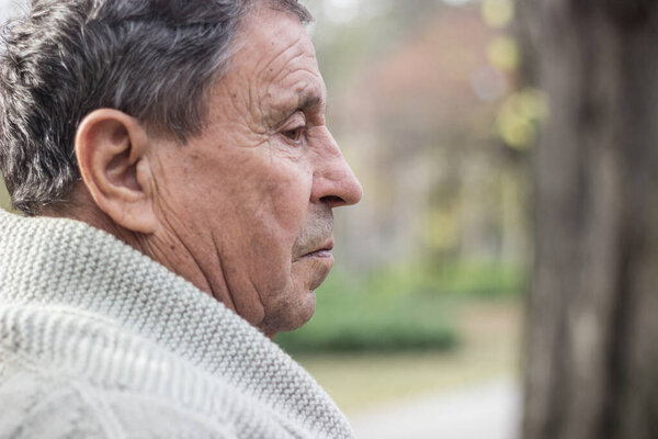 Old man relaxing outdoors and looking down. Portrait of senior man looking thoughtful