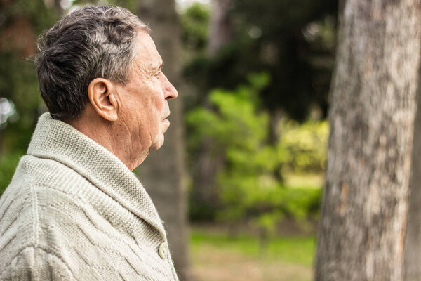 Old man relaxing outdoors and looking down. Portrait of senior man looking thoughtful