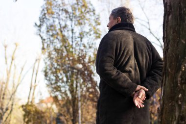 Kıdemli adam yürüyor, elleri bağlı. Kıdemli adam parkta yürüyor ve dinleniyor.