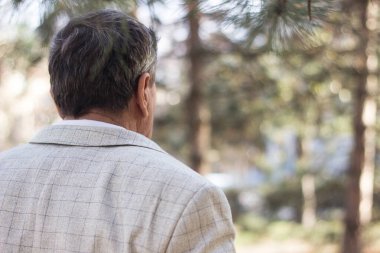 Kıdemli adam yürüyor, elleri bağlı. Kıdemli adam parkta yürüyor ve dinleniyor.